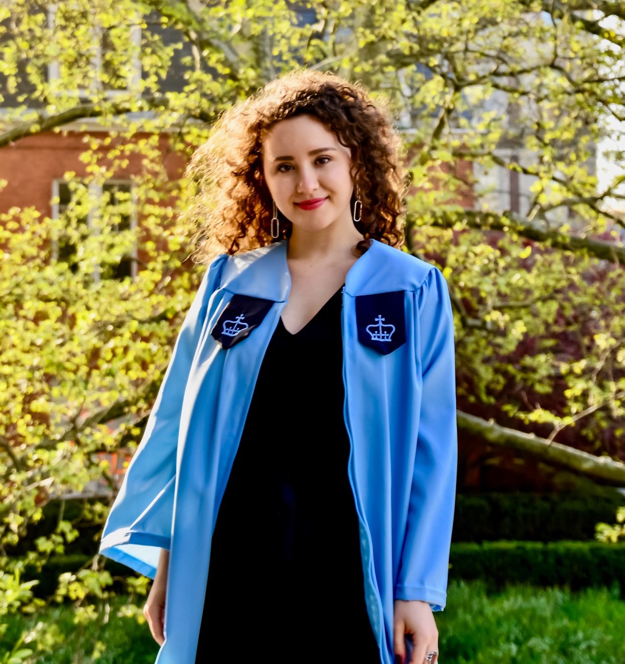 Alexandra Boubour wears a Columbia graduation gown in front of a flowering yellow tree