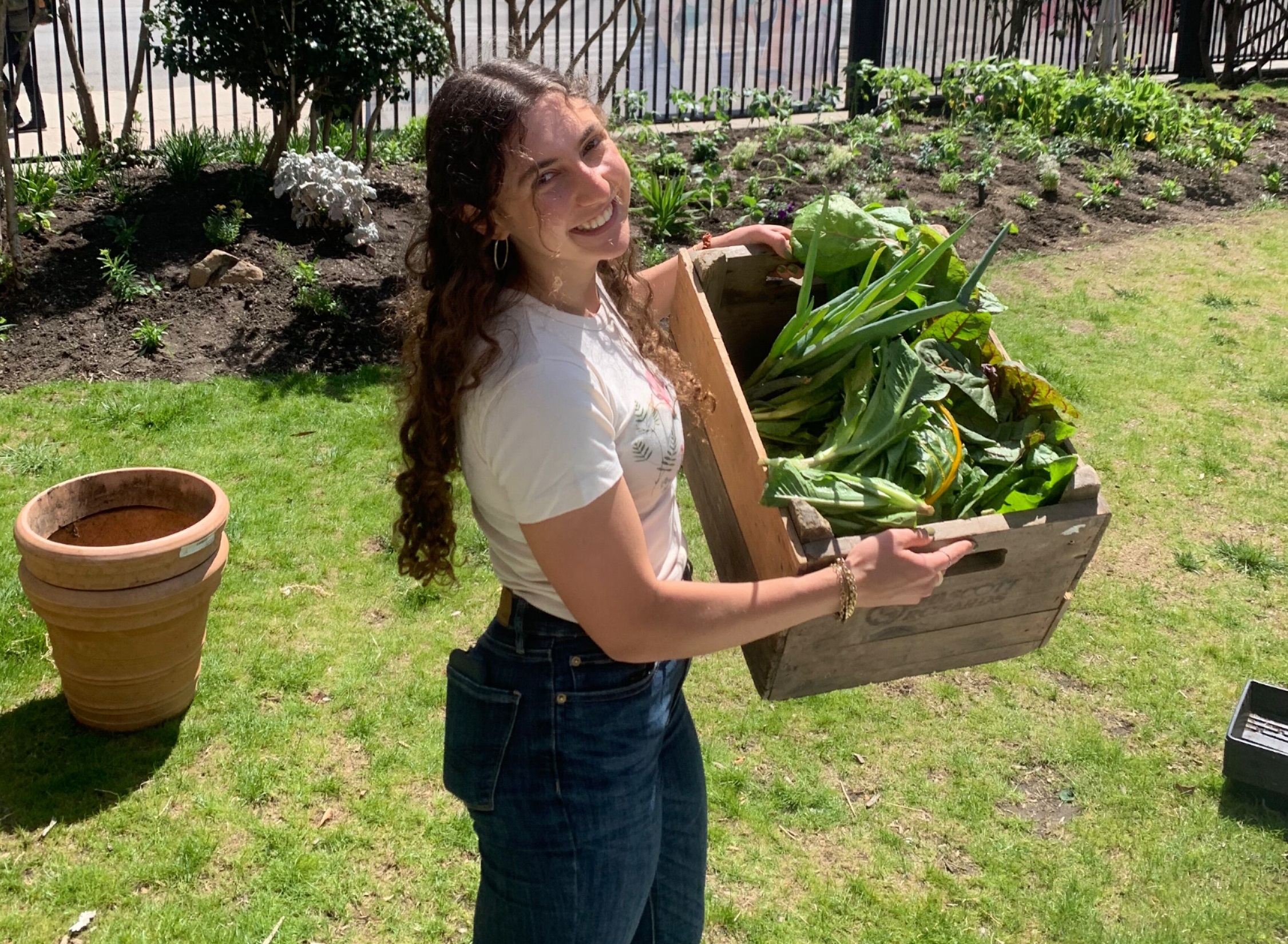Delaney Michaelson '24 poses for a photo while holding a wooden crate full of fresh greens