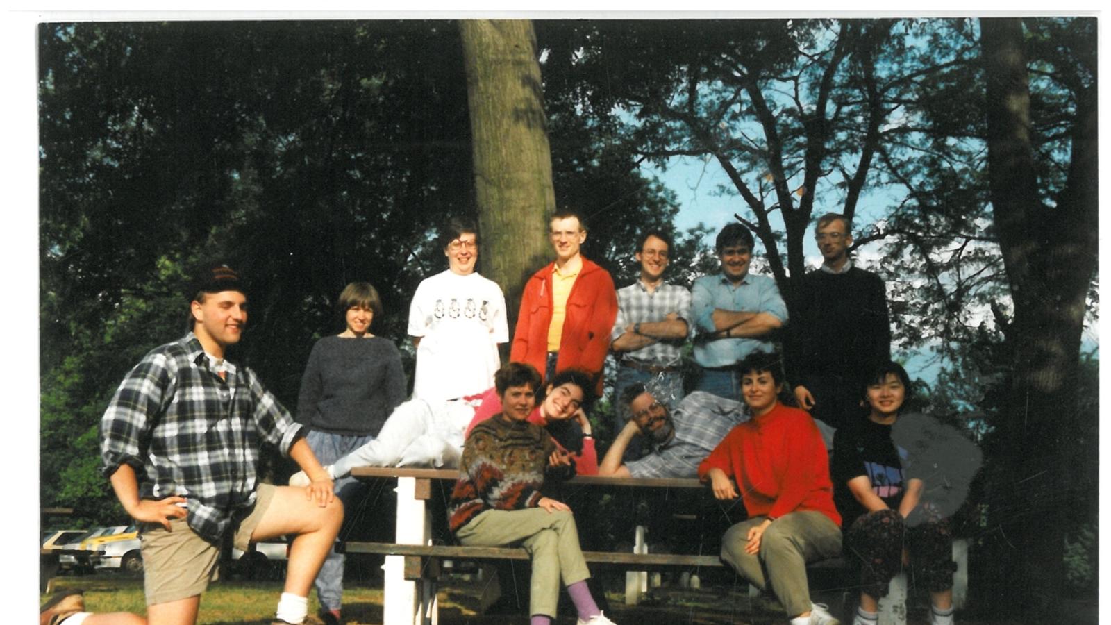 A group of researchers stands around a picnic table with trees in the background